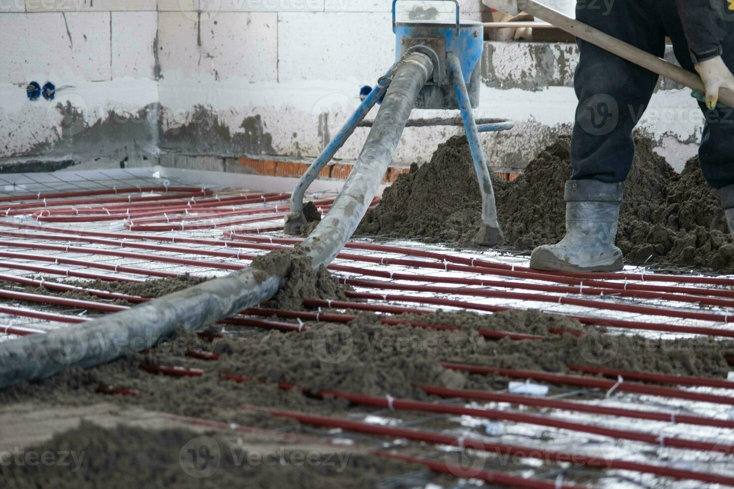 half droog verdieping dekvloer - een arbeider schoppen een bouw mengsel door een speciaal mouw voor cementeren en nivelleren Aan ondervloer verwarming pijpen. foto