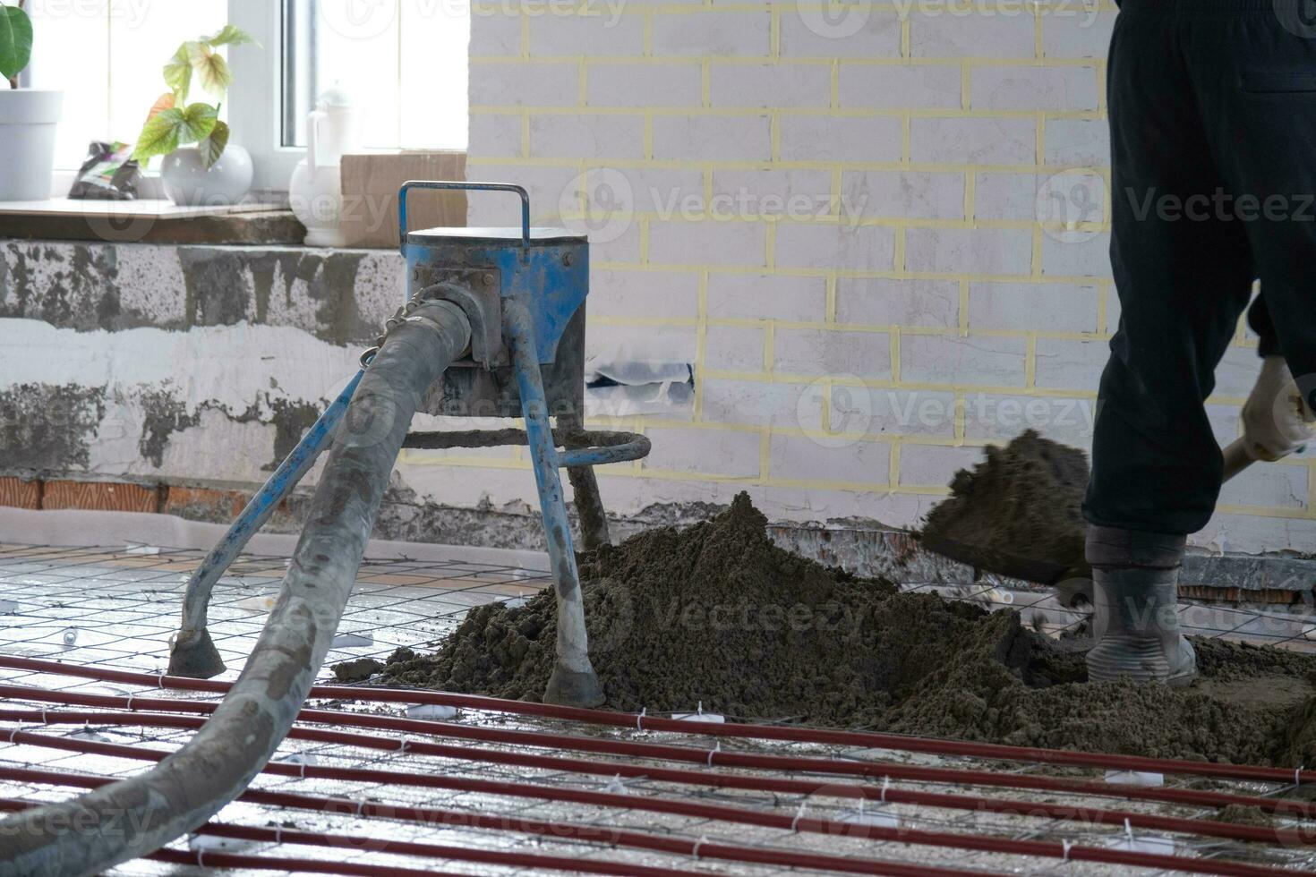 half droog verdieping dekvloer - een arbeider schoppen een bouw mengsel door een speciaal mouw voor cementeren en nivelleren Aan ondervloer verwarming pijpen. foto