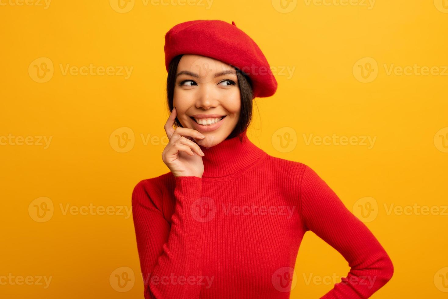 brunette meisje glimlacht met rood hoed en vest. emotioneel en blij uitdrukking. geel achtergrond foto