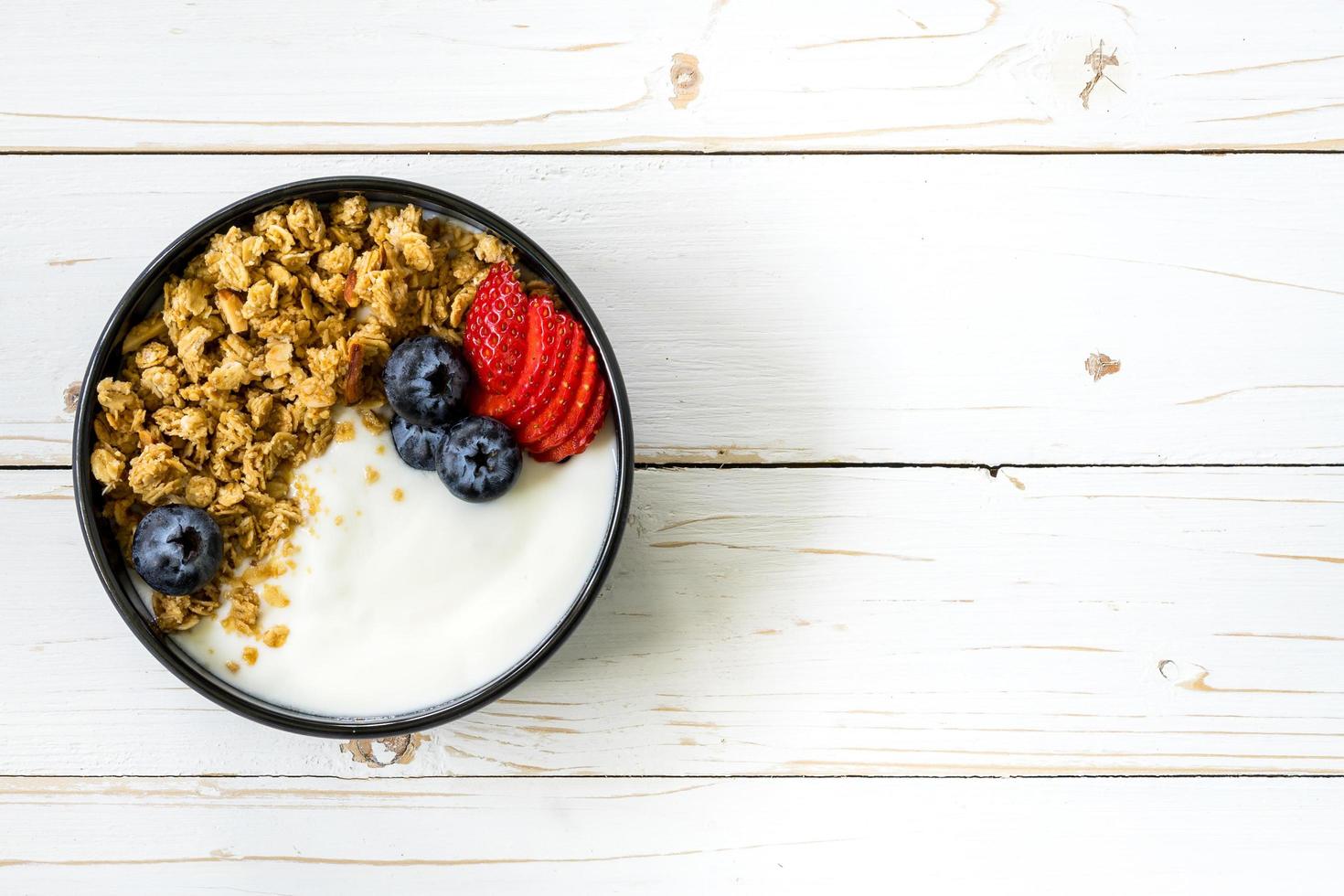 kom van muesli met yoghurt, vers bessen, aardbei Aan hout tafel. foto