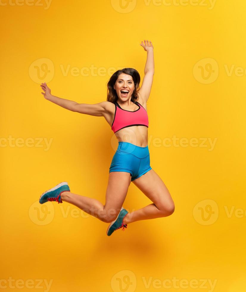 sport vrouw springt Aan een geel achtergrond. gelukkig en blij uitdrukking. foto