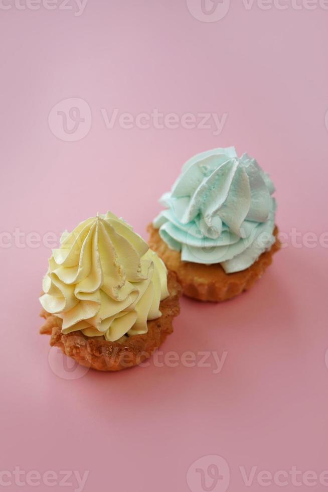 een detailopname van twee capcakes met geel en blauw room staan Aan een roze achtergrond. kopiëren ruimte. roze achtergrond. geïsoleerd. foto