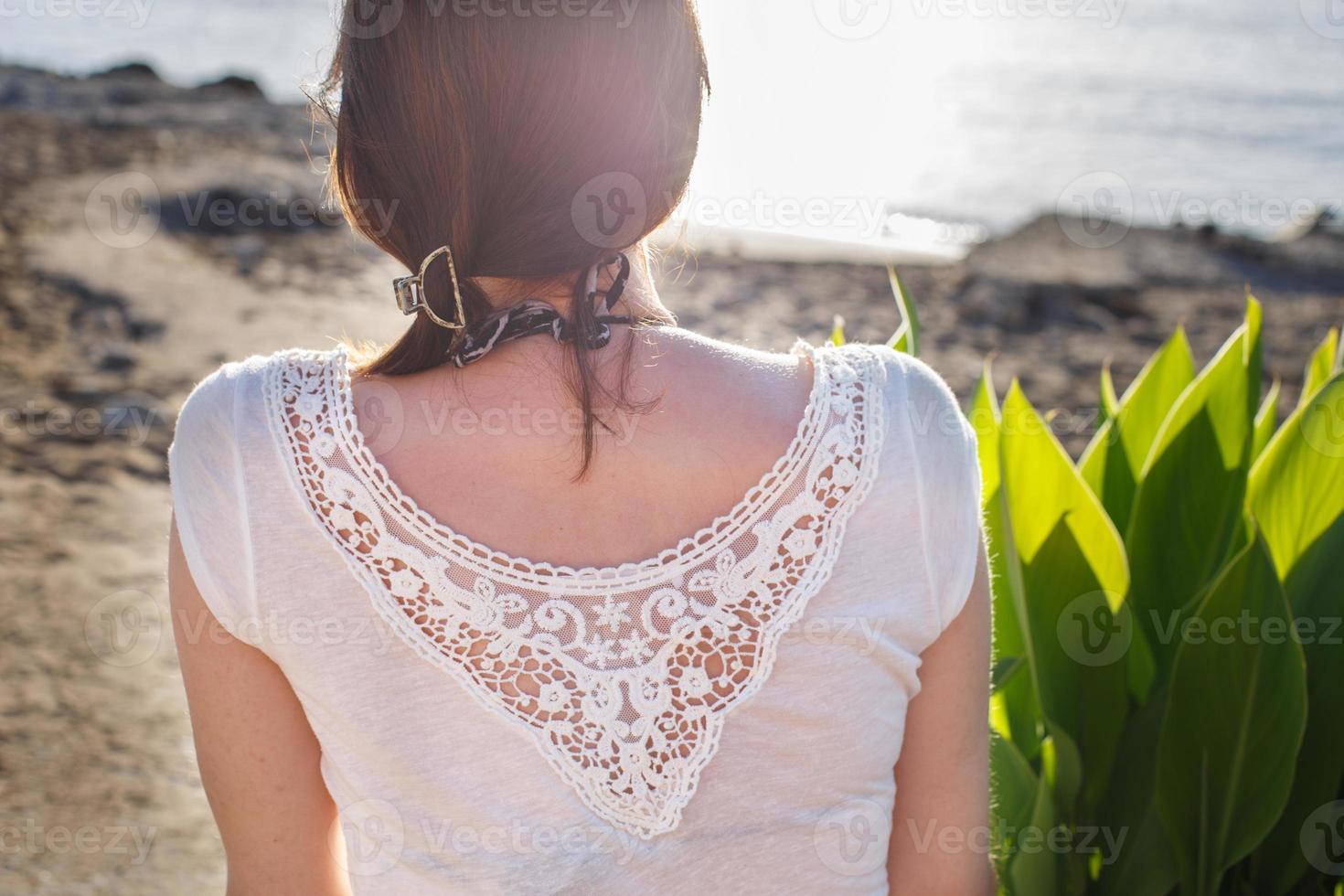 terug visie van een meisje zittend Aan zanderig strand alleen Aan de zee achtergrond dichtbij foto
