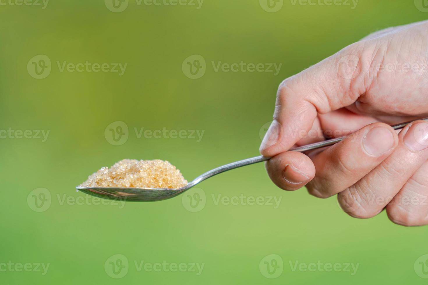 hand houdt een lepel met suiker op een natuurlijke achtergrond foto