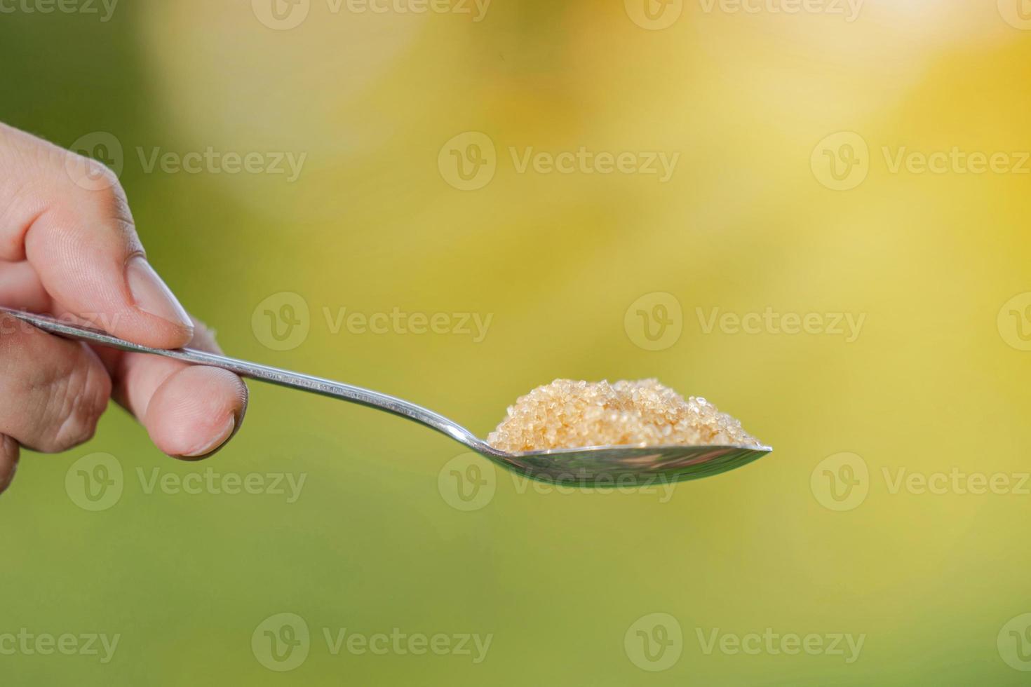 hand houdt een lepel met suiker op een natuurlijke achtergrond foto