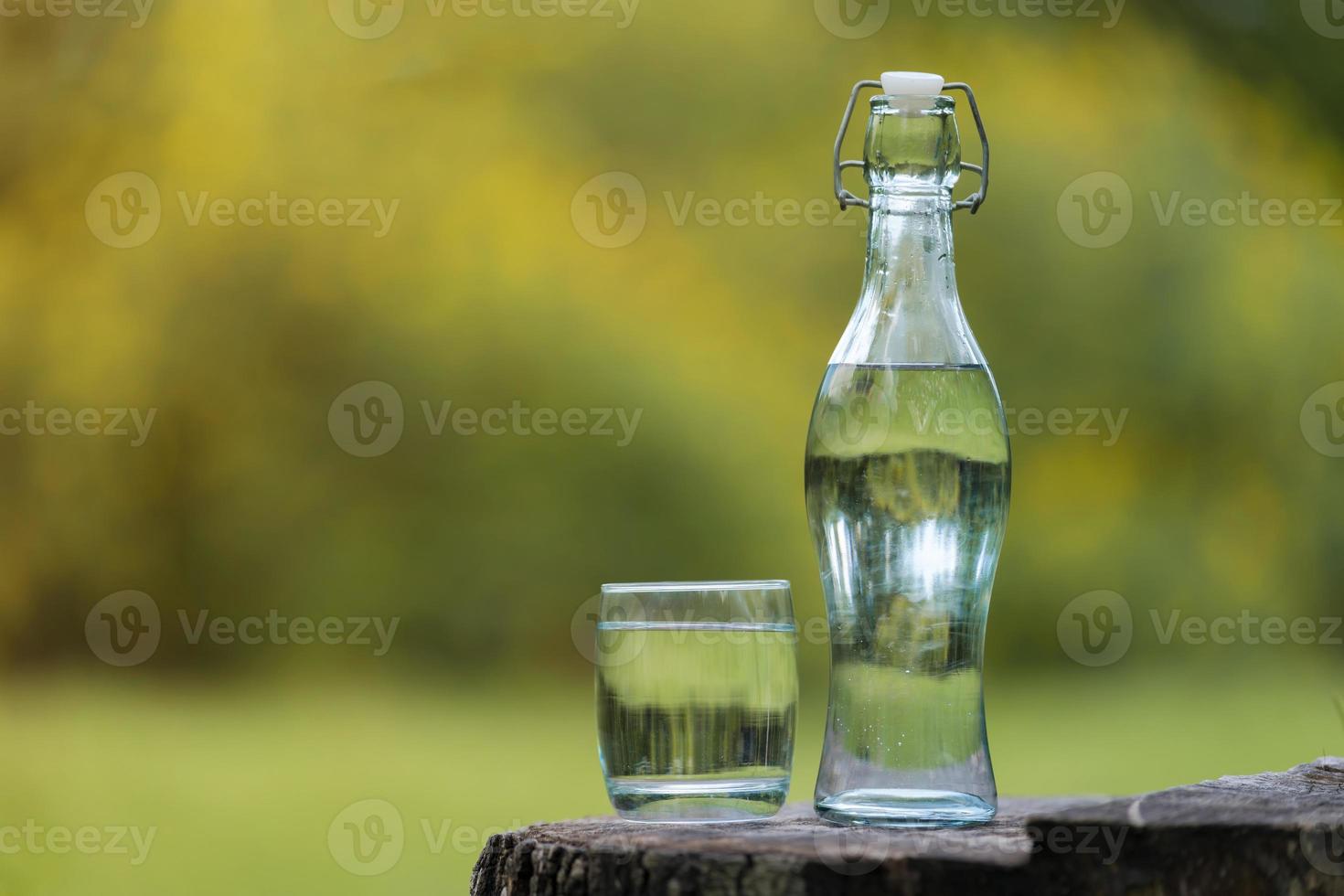 fles drinkwater en glas met natuurlijke achtergrond foto