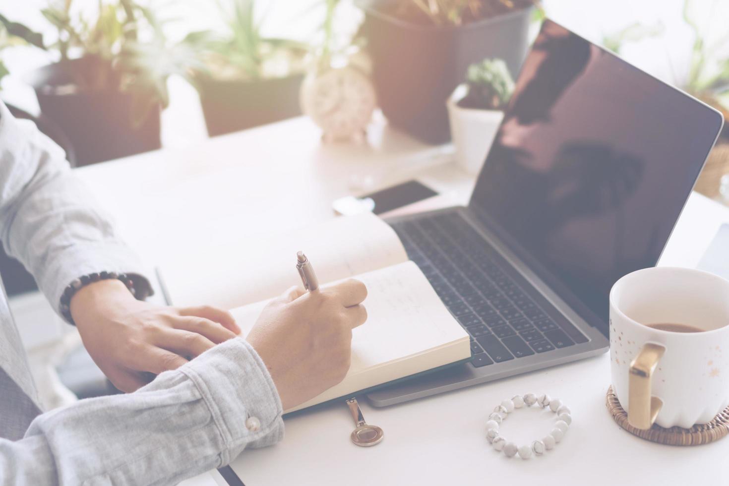 vrouw schrijven in een planner-notebook tijdens het gebruik van laptop thuis foto