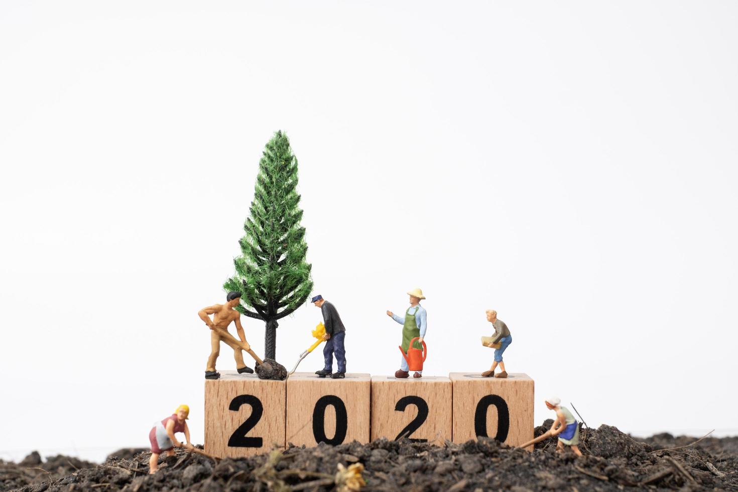 miniatuur tuinders die voor een boom op een houten blok met nummers 2020, gelukkig nieuwjaarsconcept zorgen foto