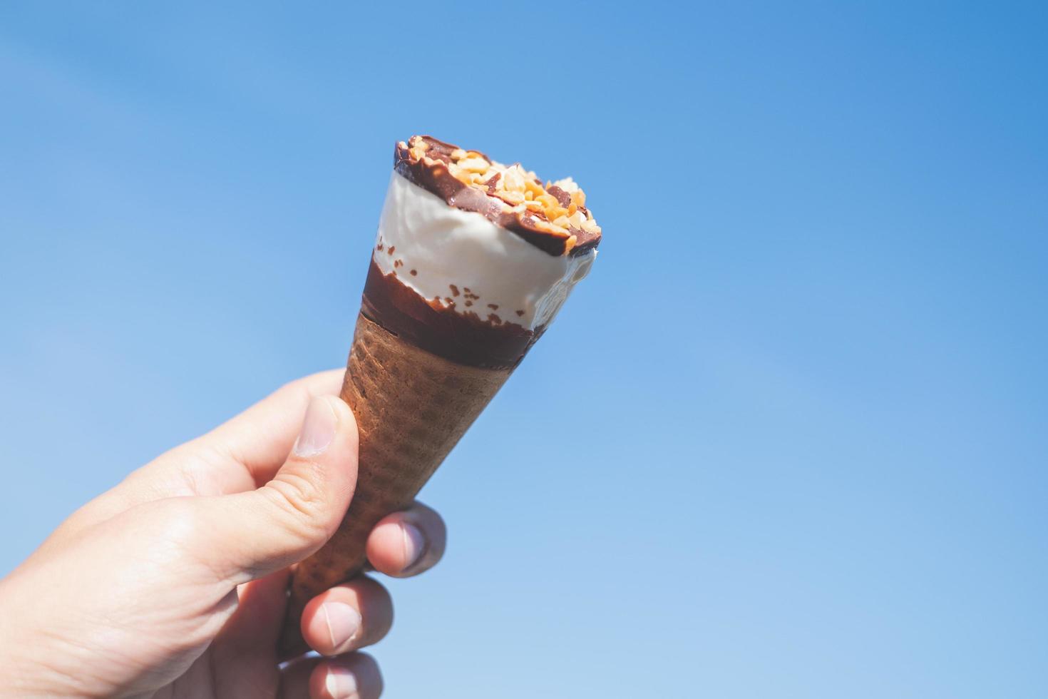 hand met een kegel van ijs met een blauwe hemelachtergrond, zomer concept foto