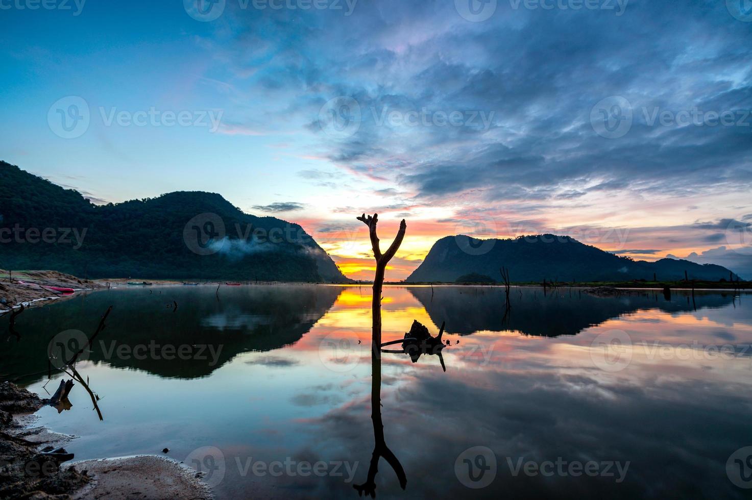 zonsopgangmening met weerspiegeling van bergen bij het reservoir van klong hua chang foto