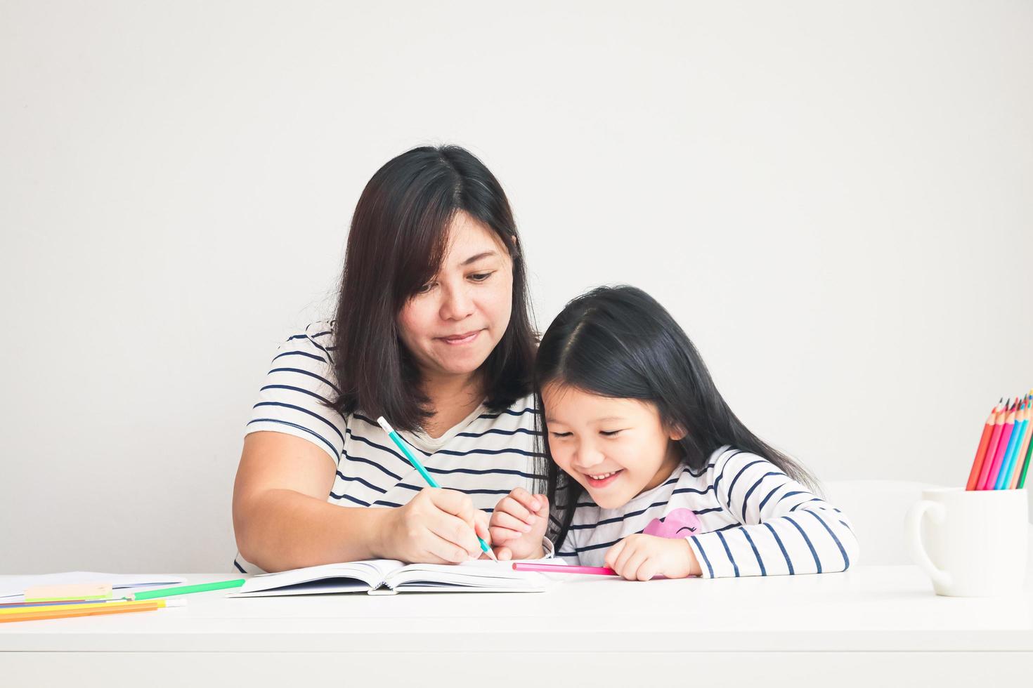 moeder onderwezen huiswerk naar de weinig dochter zittend Bij de wit tafel in de kamer. de concept van onderwijs voor elementair school- kinderen foto