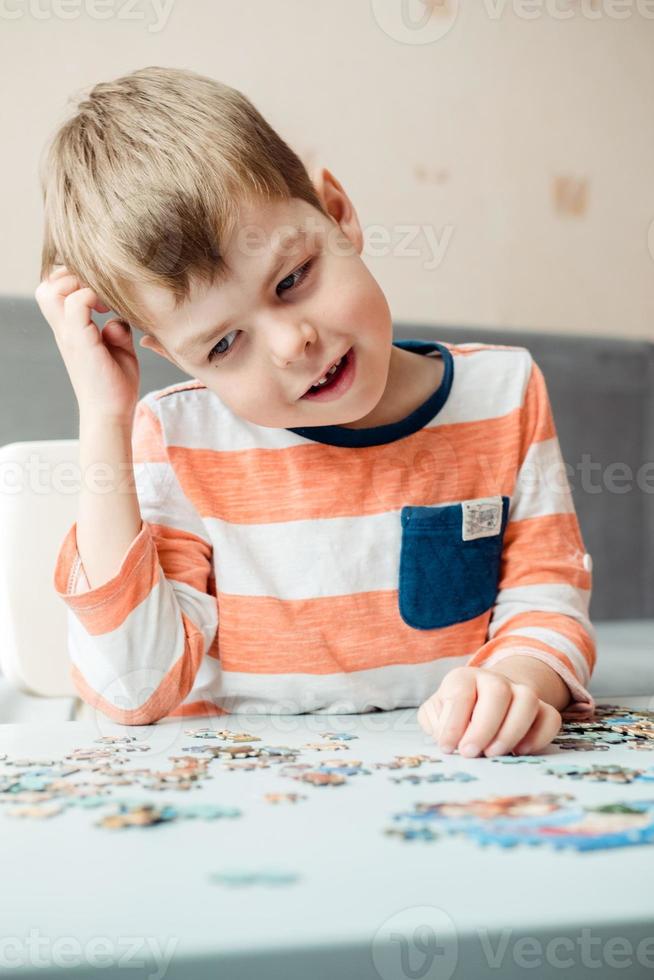 een 6 jaar oud jongen verzamelt een puzzel Bij huis en houdt zijn hoofd. ontwikkeling van prima motor vaardigheden en de hersenen foto