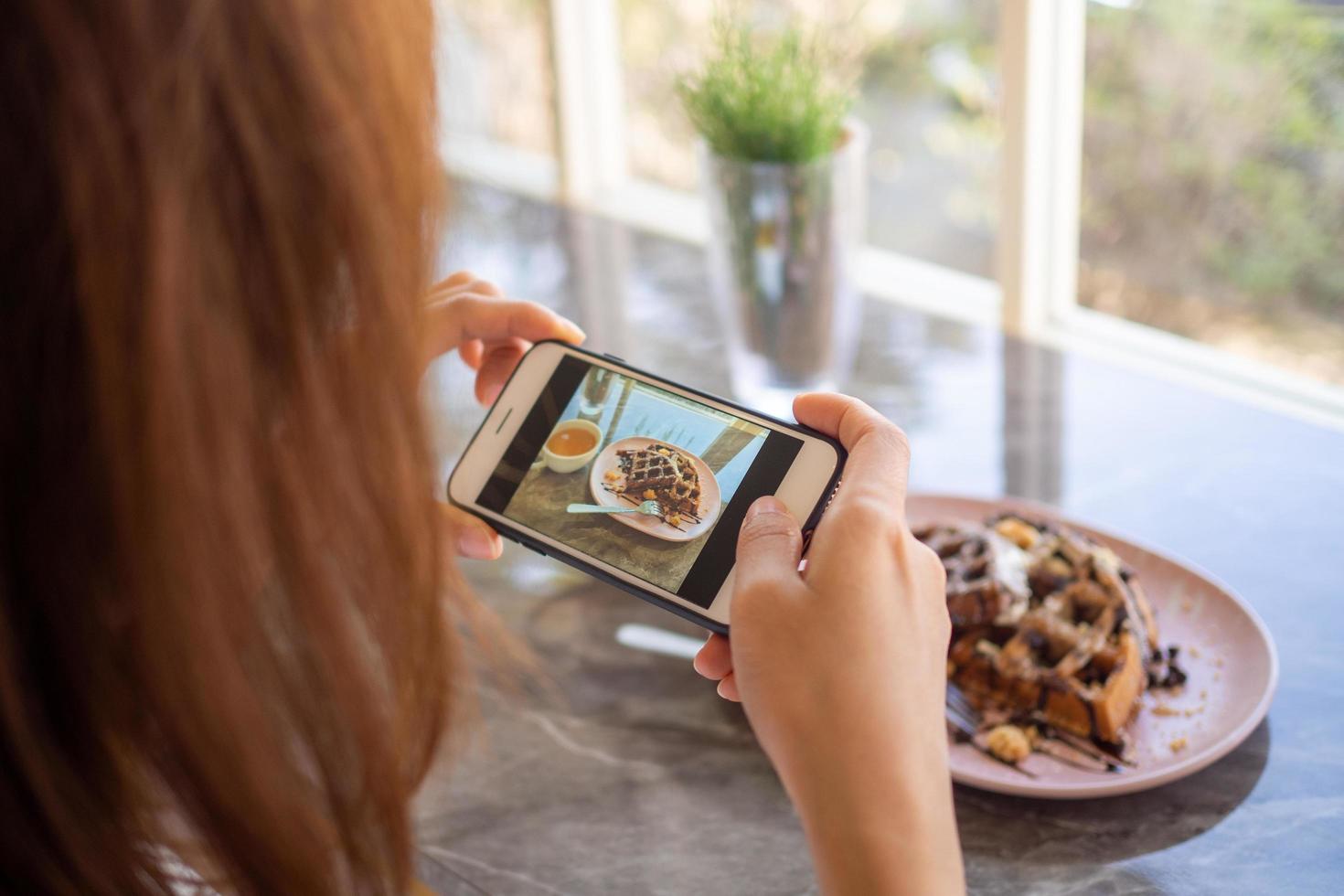 de vrouw hand- nam een foto van de met chocolade bedekt wafels in de koffie winkel en bereid naar uploaden naar een sociaal app
