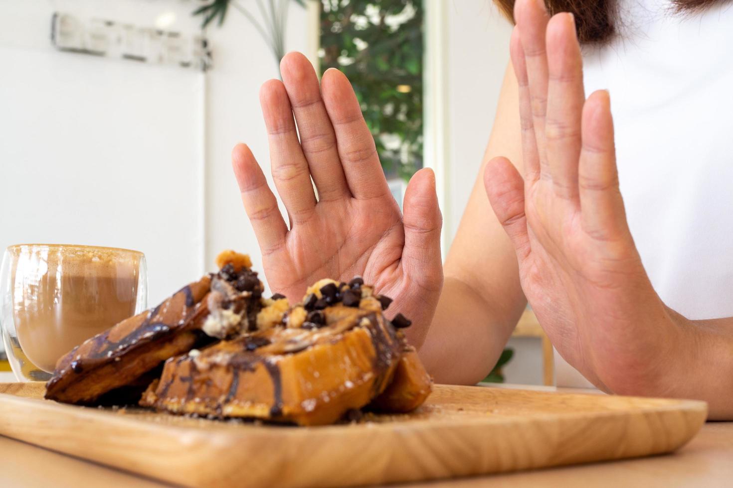 een van de gezondheidszorg meisjes gebruikt een hand- naar Duwen een bord van chocola taart. weigeren naar eten voedingsmiddelen dat bevatten trans dik. foto