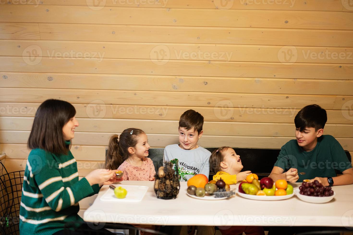 moeder met vier kinderen eten fruit in houten land huis Aan weekend. foto