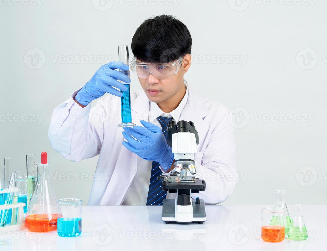 Aziatisch mannetje leerling wetenschapper in reagens menging laboratorium in een wetenschap Onderzoek laboratorium met test buizen van divers maten en microscopen. Aan de tafel in laboratorium chemie laboratorium wit achtergrond. foto