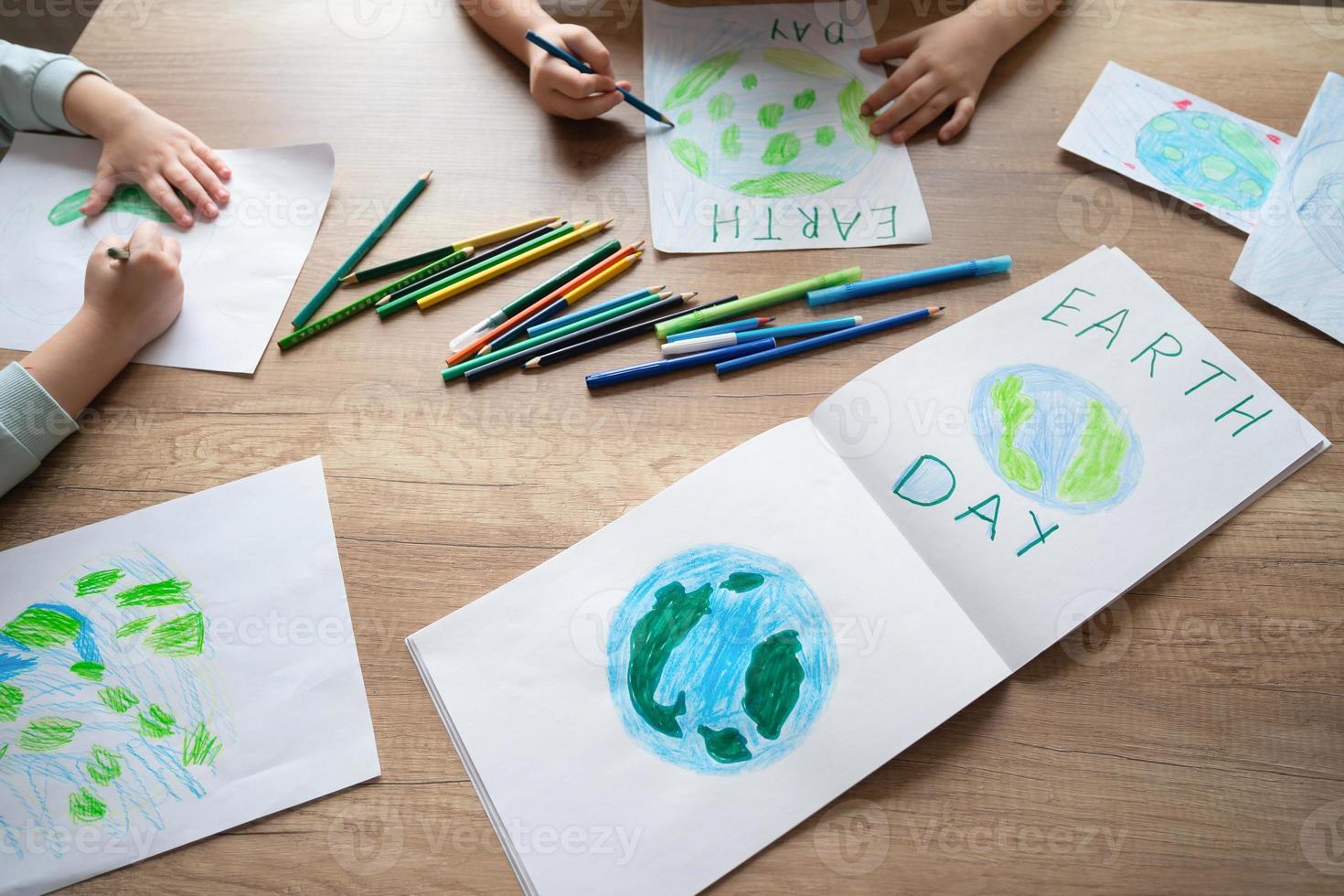 kinderen trek de planeet aarde met potloden en viltstift pennen Aan album lakens voor aarde dag Bij hun huis tafel. de concept van beschermen de omgeving, vrede Aan aarde. foto