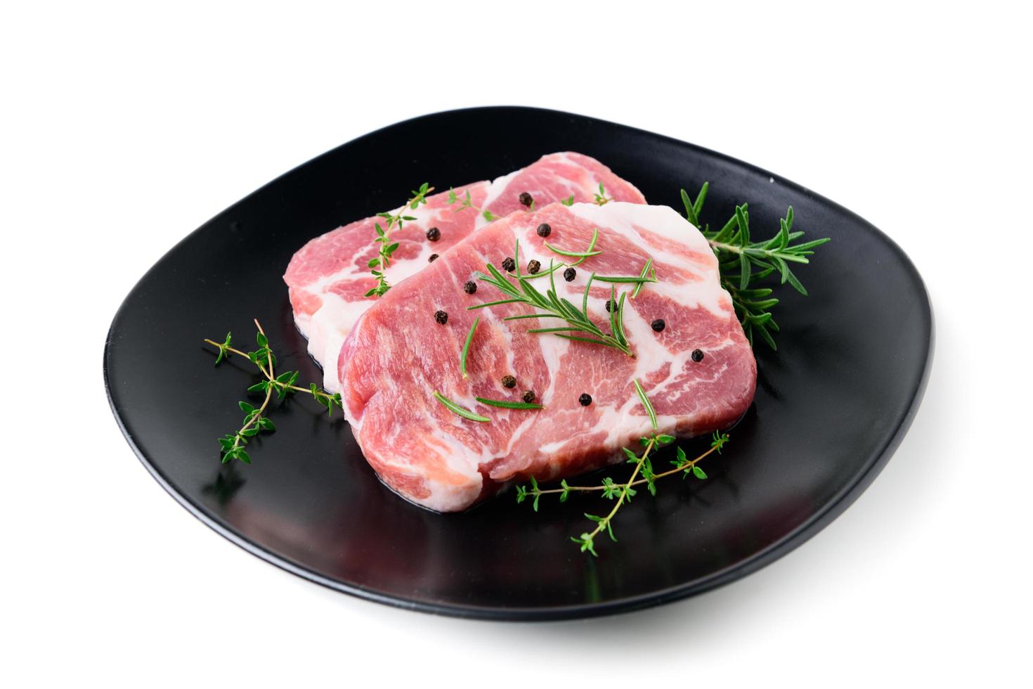 stukken van varkensvlees vlees met rozemarijn en tijm bladeren Aan zwart schotel Aan wit achtergrond, foto
