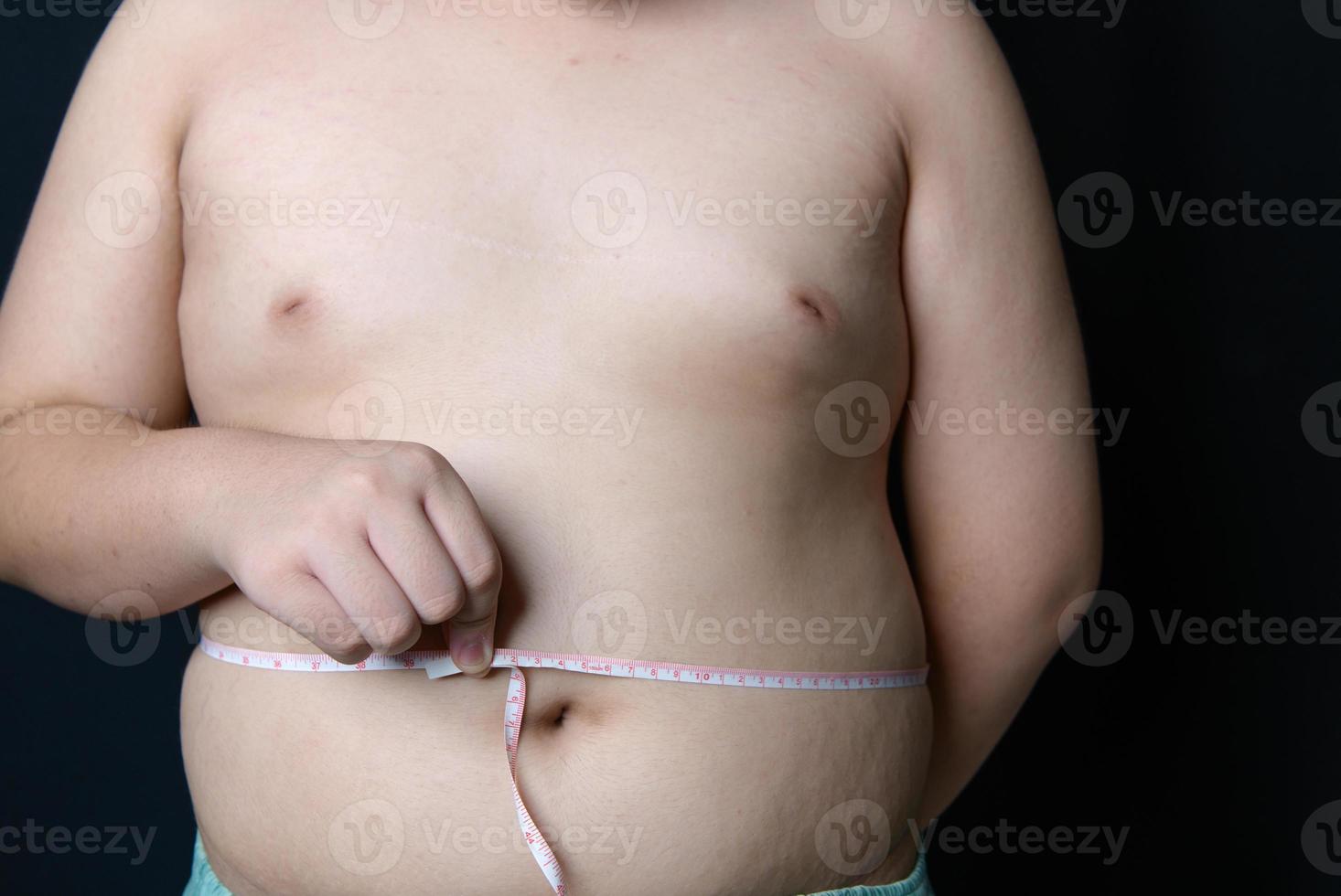 zwaarlijvig dik jongen meten plakband van maag geïsoleerd Aan zwart achtergrond, gezond en verliezen gewicht foto
