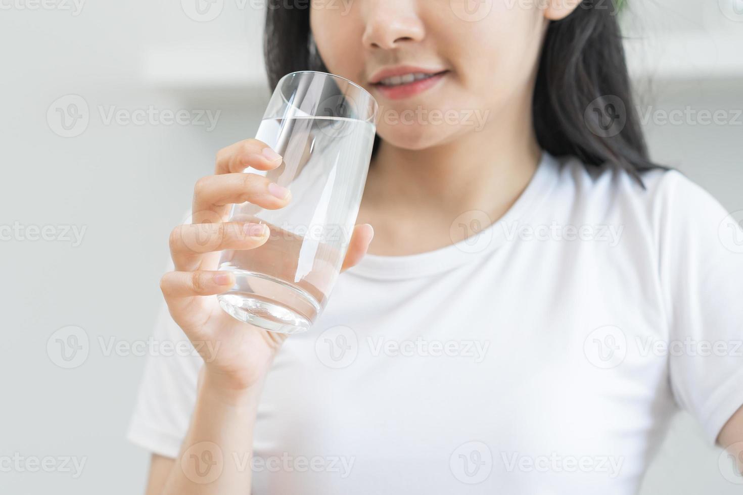 gelukkig mooi, Aziatisch jong vrouw hand- in vasthouden, drinken vers glas van water voor hydratatie van lichaam, Holding transparant glas in haar hand, dorstig Bij huis. Gezondheid zorg, gezond levensstijl concept. foto