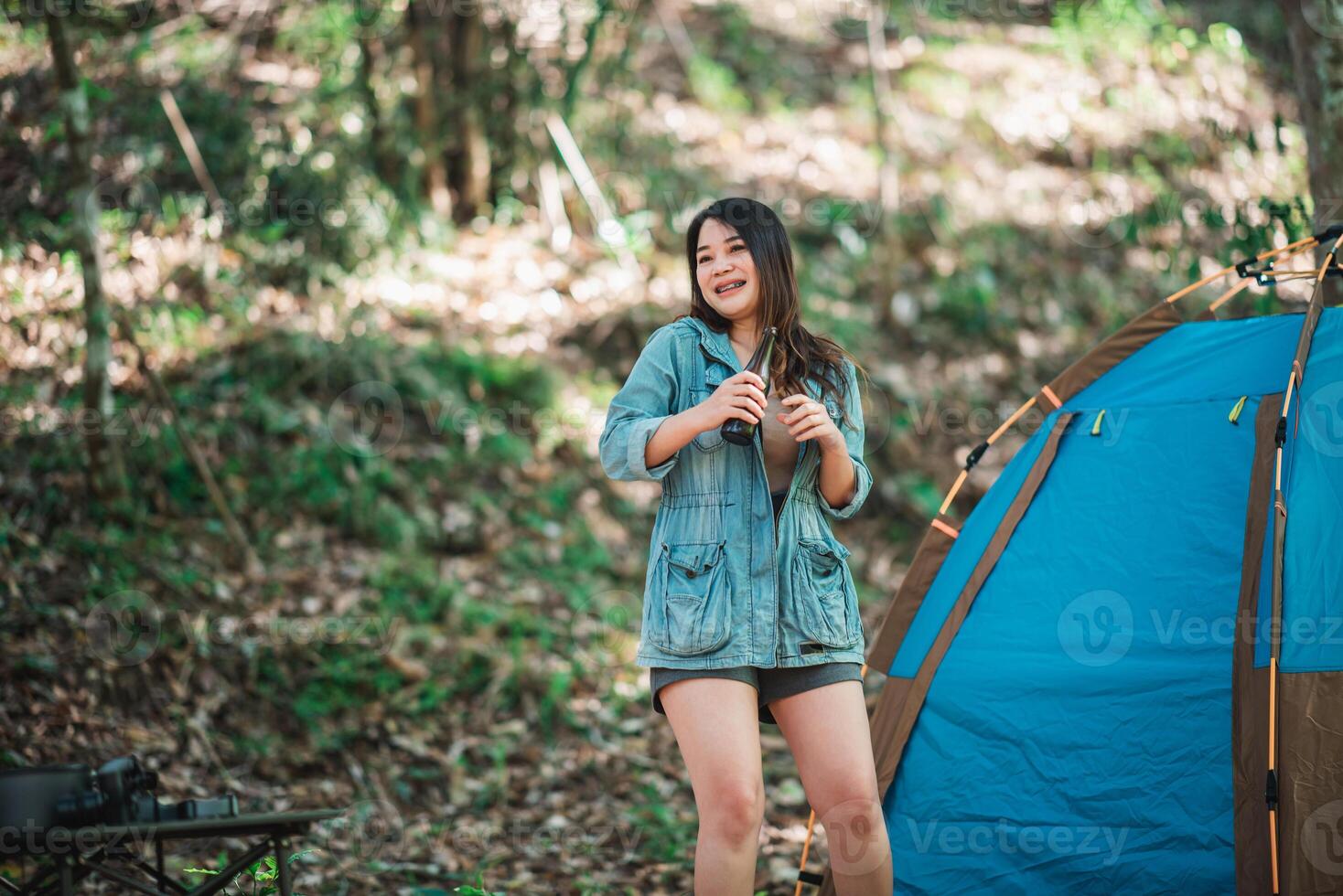 jong vrouw juichen en drinken drank voorkant van camping tent foto