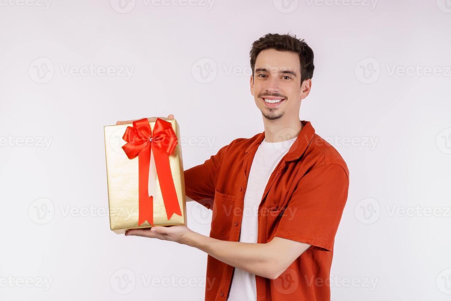 portret van gelukkig jong Kaukasisch Mens tonen Cadeau doos en op zoek Bij camera geïsoleerd over- wit achtergrond foto