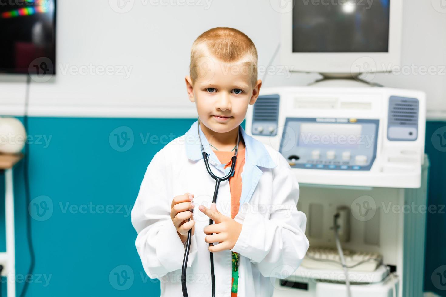 glimlachen weinig jongen in medisch uniform Holding stethoscoop en op zoek Bij camera foto
