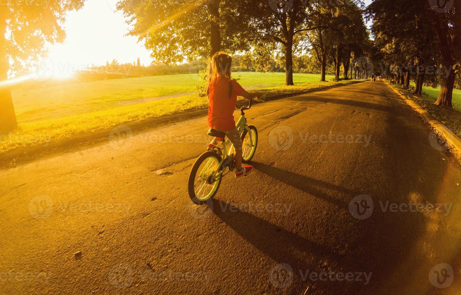 weinig meisje met rijden fiets Bij zonsondergang foto