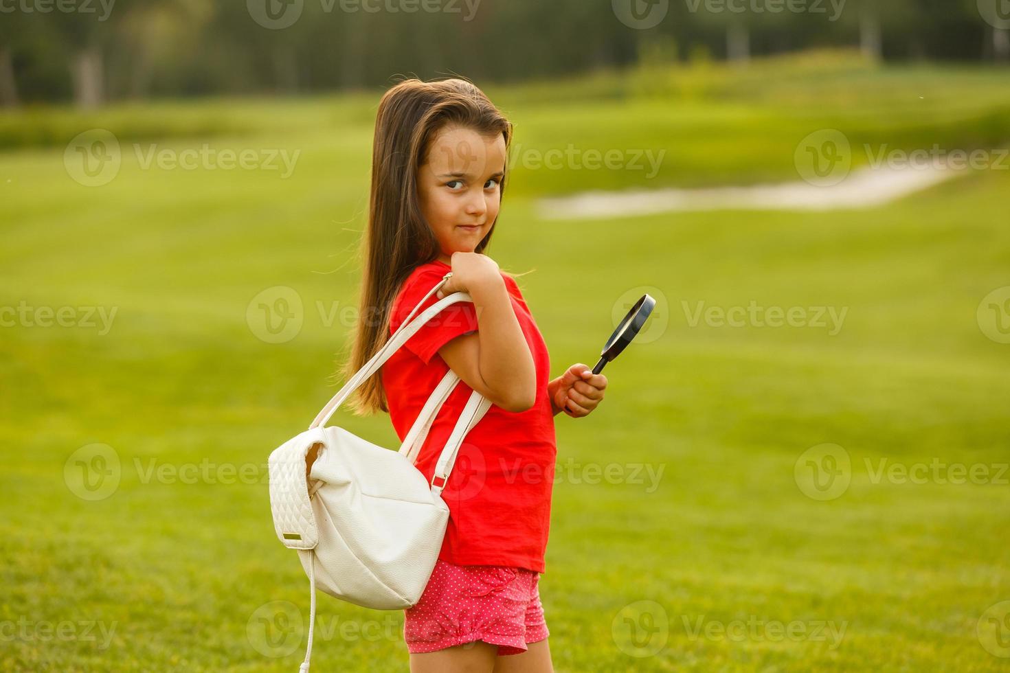 mooi weinig meisje met vergroten glas in zomer park foto