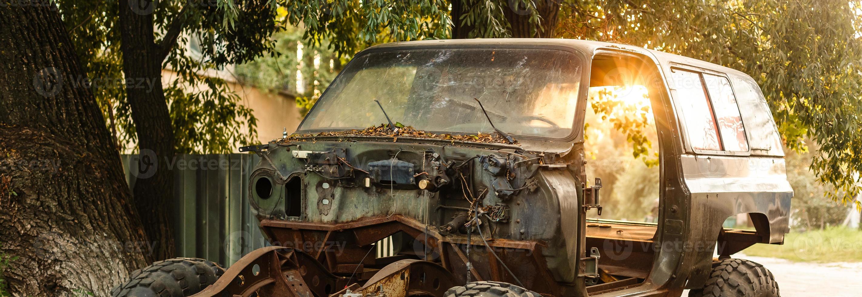 detailopname van een oud roestig auto met een gebroken deur en Nee wielen Aan de achtergrond van een groen naald- Woud foto