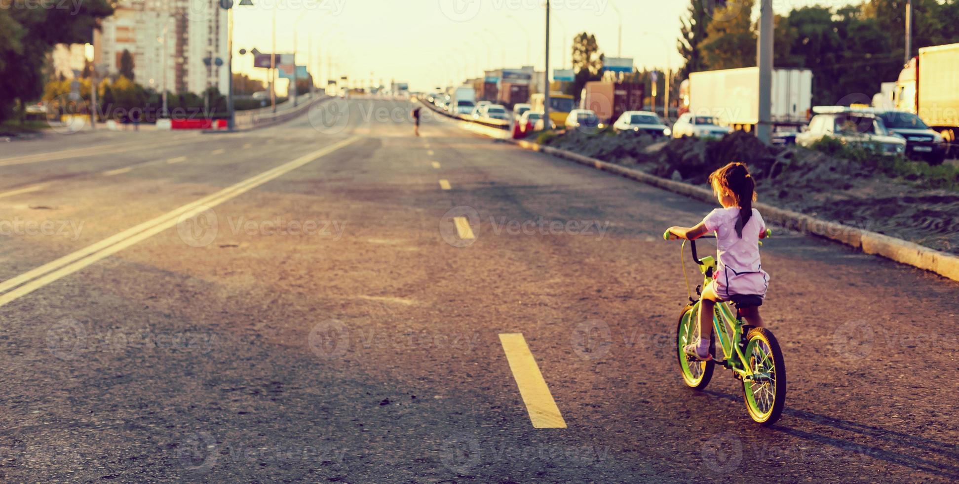 weinig brunette meisje rijden fiets Aan weg Bij zonsondergang foto