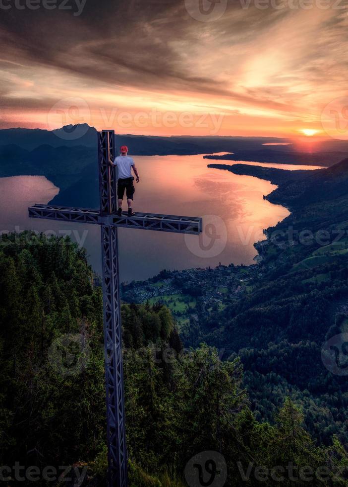 een reusachtig kruis Aan een berg met een Mens staand Aan het gedurende zonsondergang foto