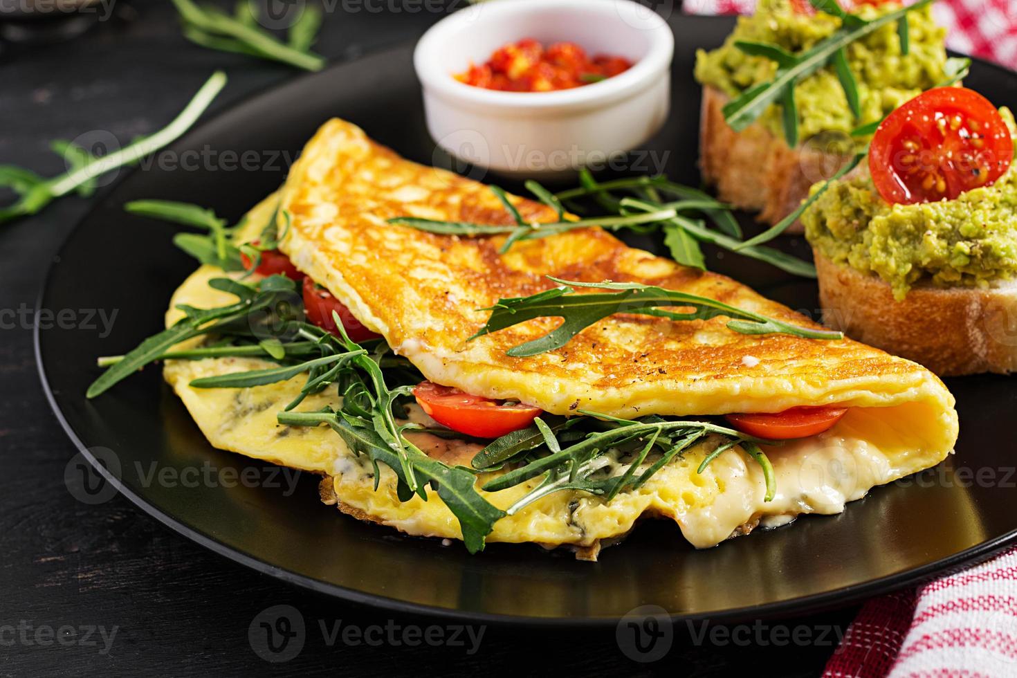 ontbijt. omelet met tomaten, kaas, groen rucola en toast met avocado room Aan zwart bord. frittata - Italiaans omelet. foto