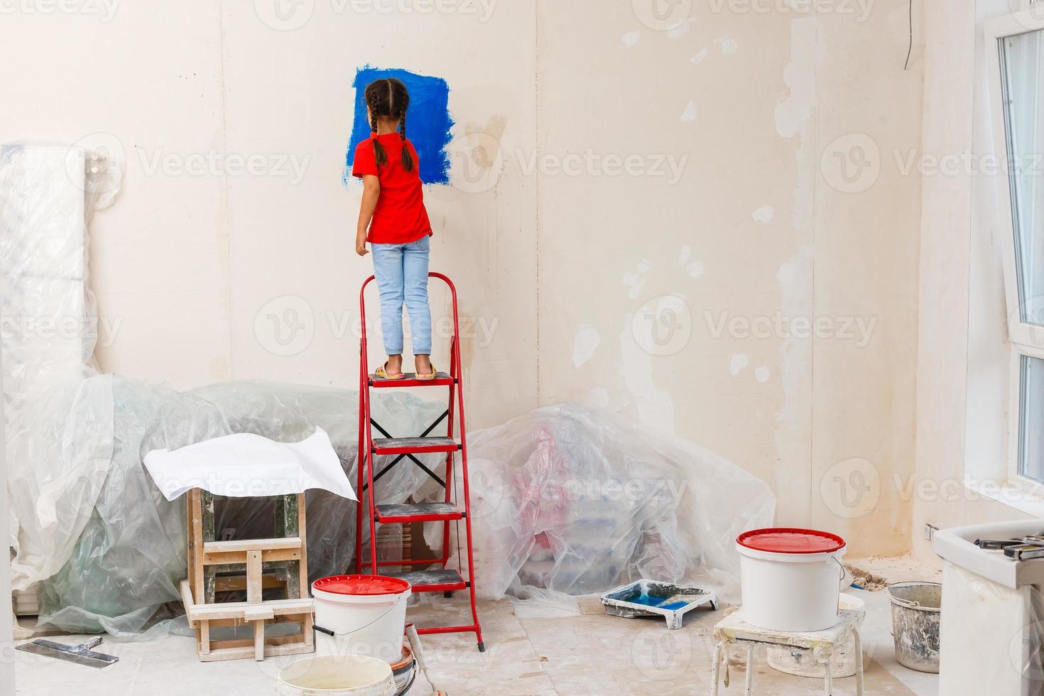 reparatie in de appartement. gelukkig kind meisje verven de muur met blauw verf foto