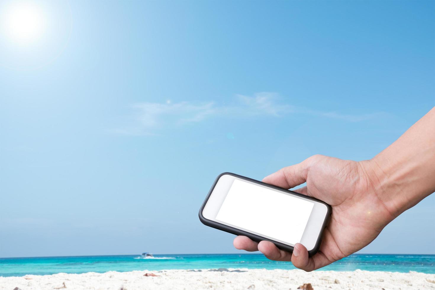 hand met een smartphone over een strand en een blauwe hemelachtergrond foto