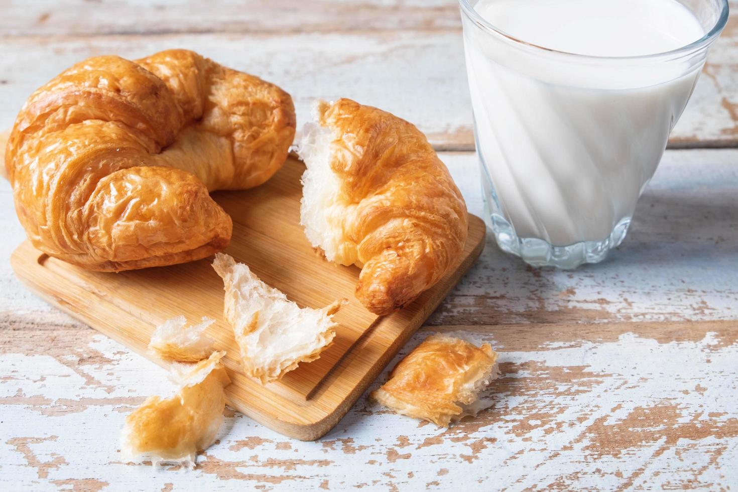 croissants op een houten snijplank naast glas melk op blauwe houten tafel foto