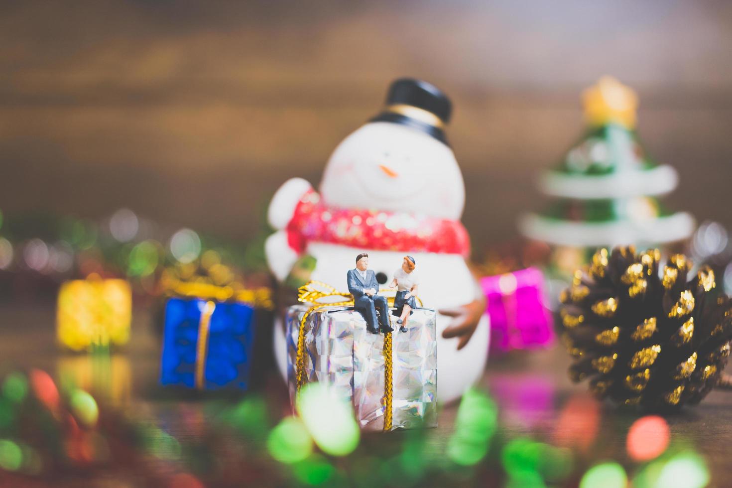 miniatuurmensen op een geschenkdoos met kerstvieringsdecoratie op de achtergrond foto