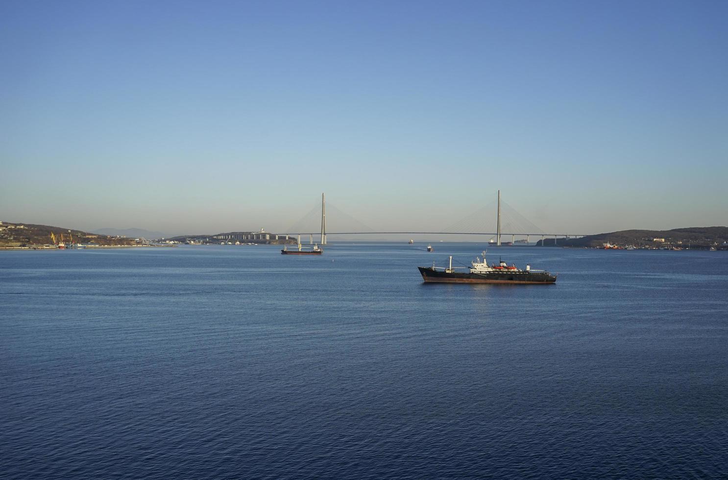 zeegezicht met schepen in water en de russky brug tegen een heldere blauwe hemel in Vladivostok, Rusland foto