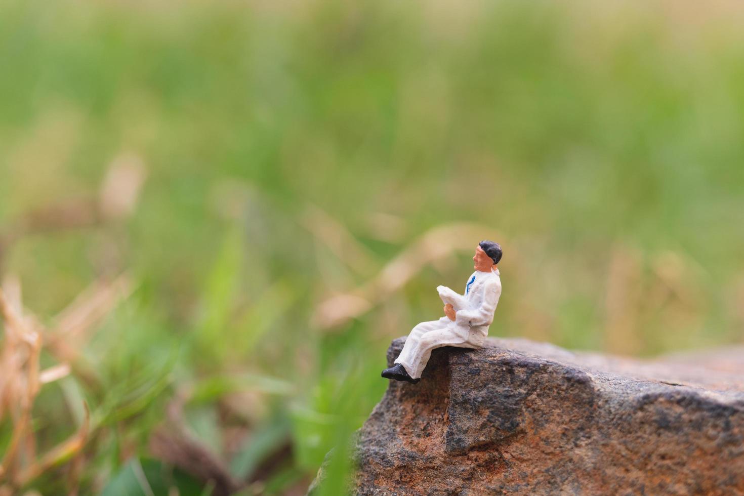 miniatuurzakenman die een krant op een rots met een aardachtergrond leest foto