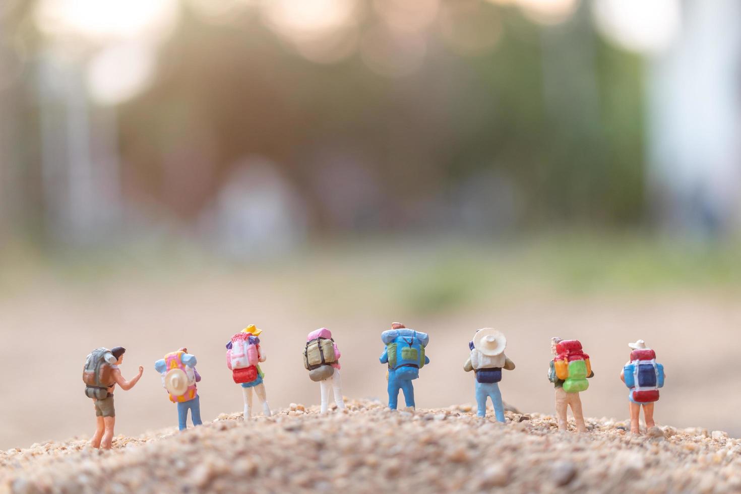 miniatuurreizigers met rugzakken die op zand, reis en avontuurconcept lopen foto