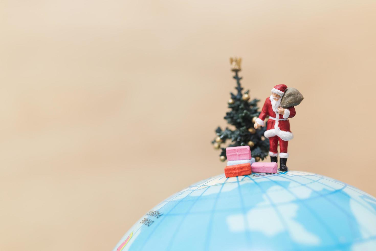 miniatuur kerstman met geschenken voor kinderen op een wereldbol, vrolijk kerstfeest concept foto