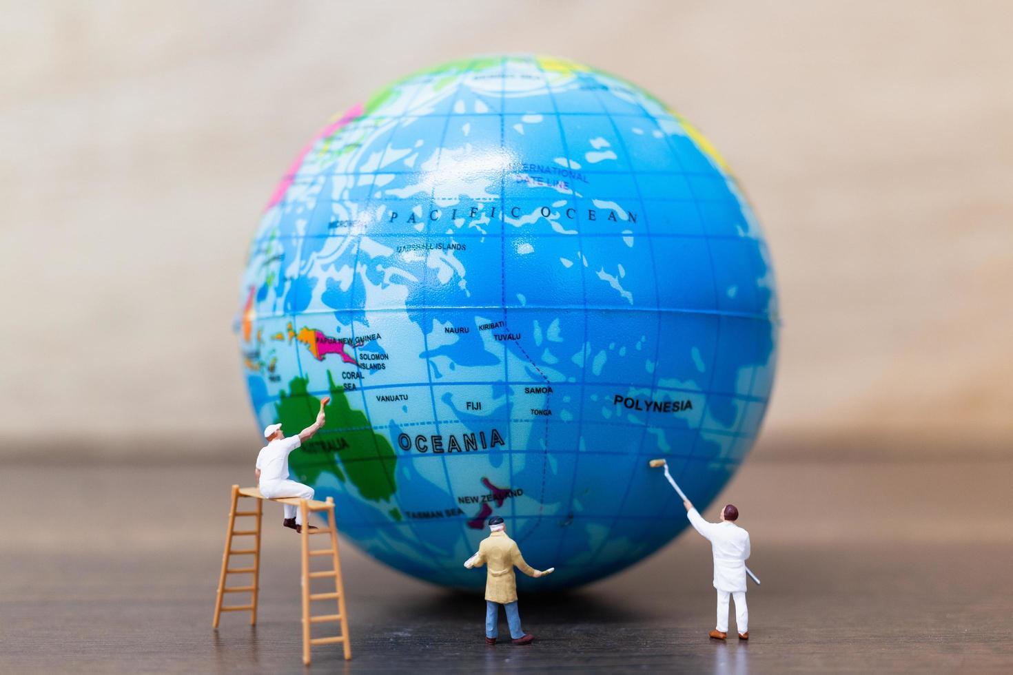 miniatuurschilders die op een wereldbol met een houten achtergrond schilderen, sparen het aardeconcept foto