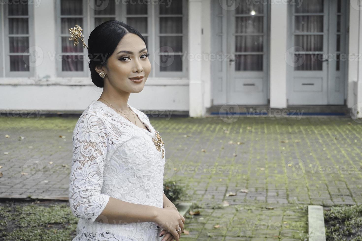 een jong Indonesisch vrouw met een gelukkig geslaagd uitdrukking vervelend een wit kebaya. kartini's dag concept. foto