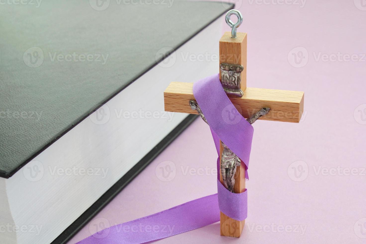 christen religieus houten kruis kruisbeeld met paars lint en Bijbel boek Aan Purper achtergrond. Katholiek religie symbool. mooi zo vrijdag, vasten seizoen, palm zondag, as woensdag en heilig week concept foto