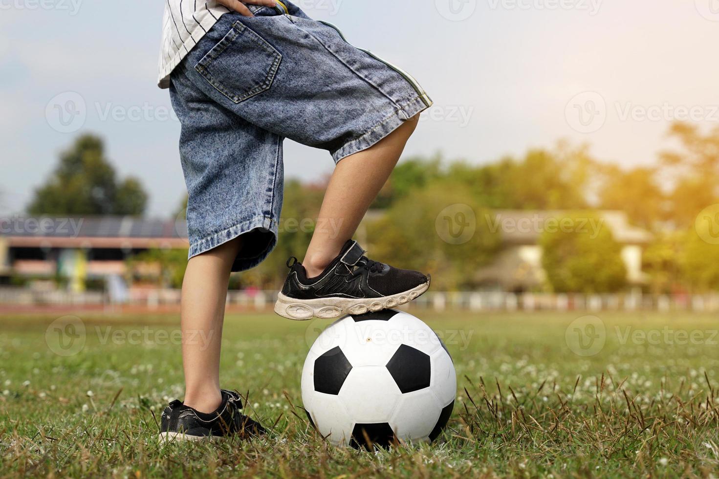 Aziatisch jongen stepping Aan een bal terwijl schoppen voetbal Aan de veld. zacht en selectief focus. foto