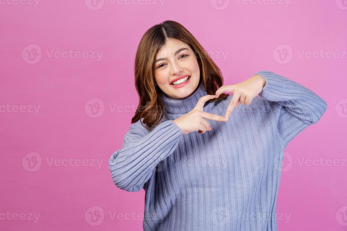 portret van glimlachen jong vrouw voelt gelukkig en romantisch vormen hart gebaar geïsoleerd over- roze achtergrond foto