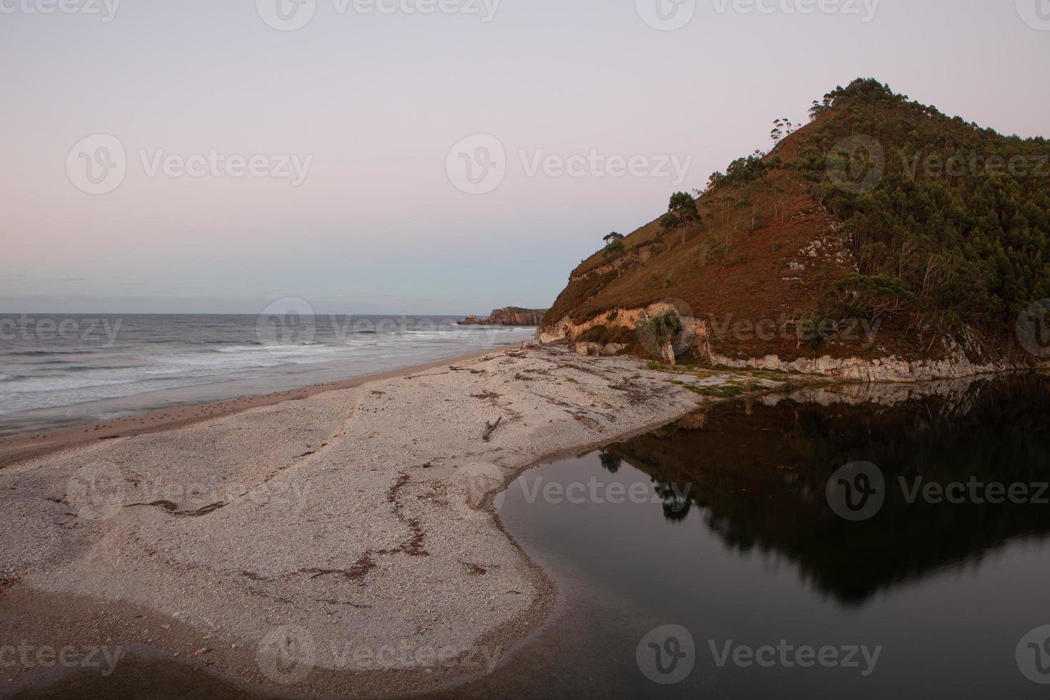 strand met bergen op de achtergrond en warm zonsonderganglicht foto