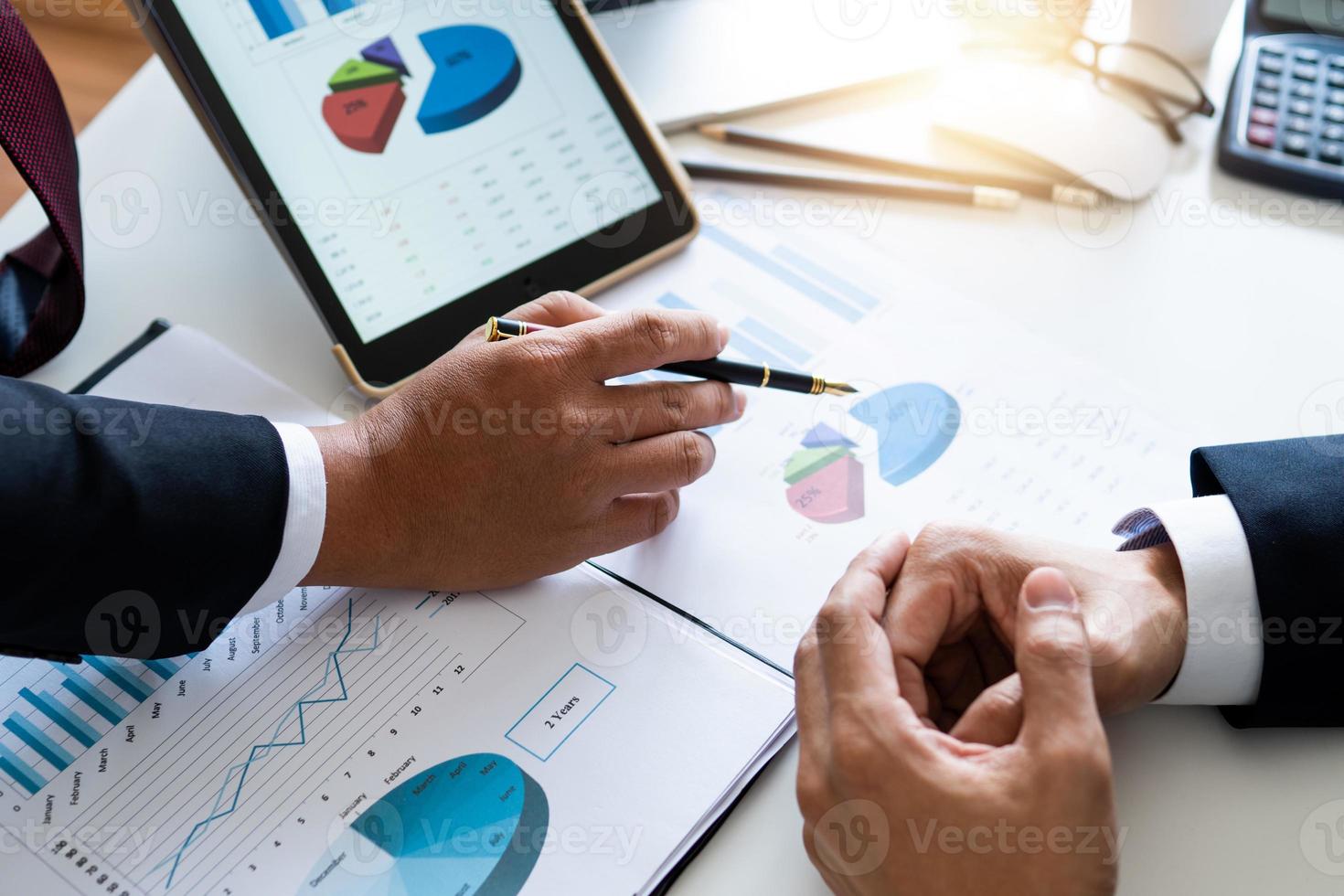 close-up van twee zakenlieden handen naast grafieken en grafieken op papier en tablet foto