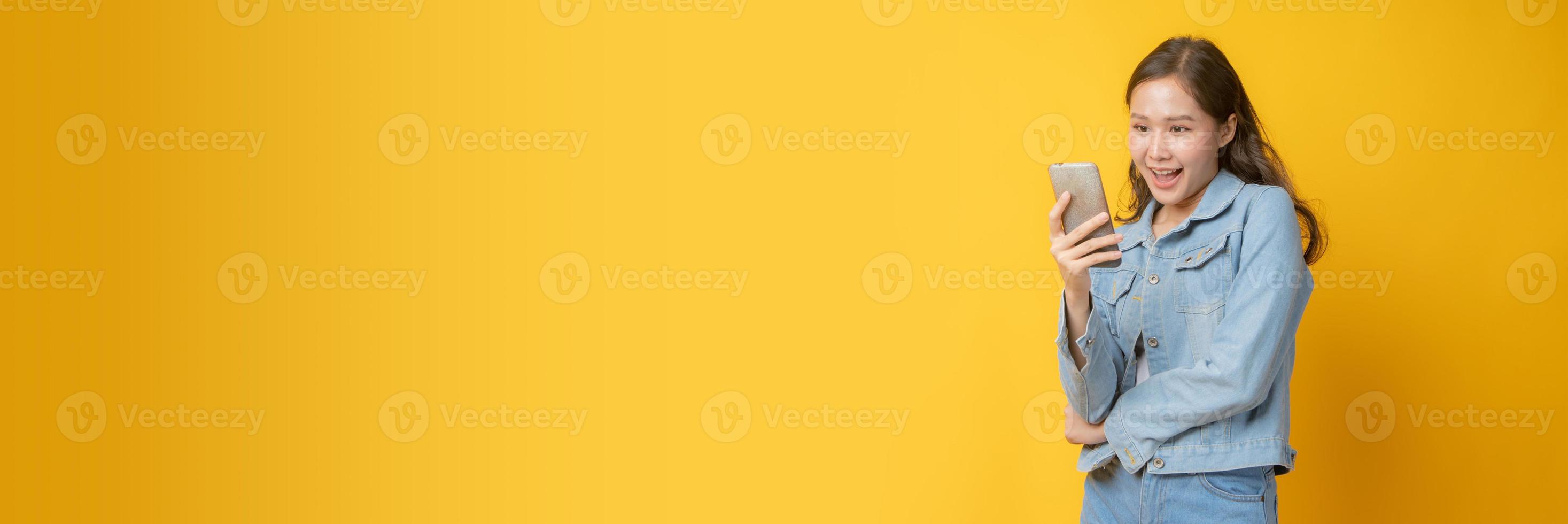 Aziatische vrouw glimlachend en kijken naar mobiele telefoon op gele achtergrond foto