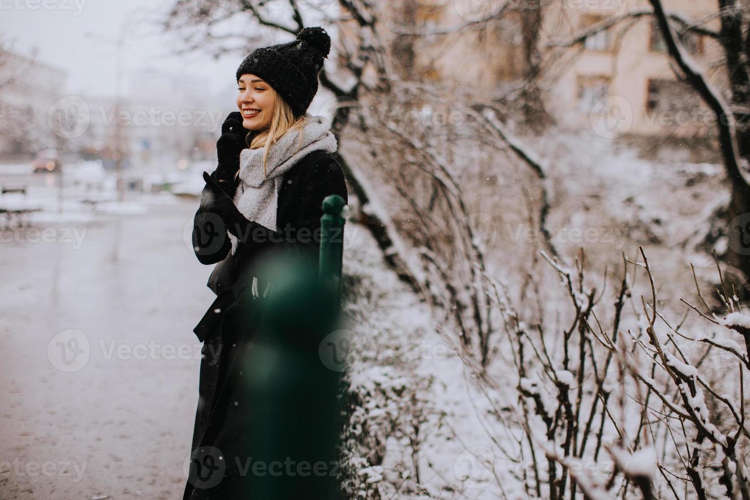 jong vrouw in warm kleren gebruik makend van mobiel telefoon Aan een winter dag foto